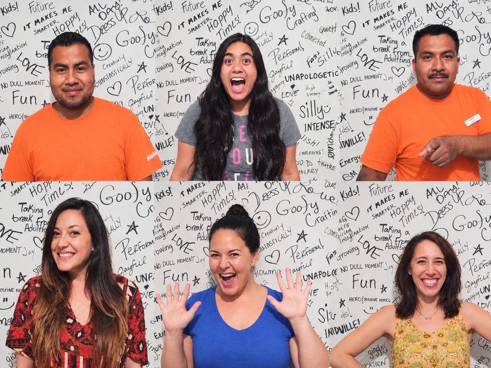 Kidville team members smiling in front of a handwritten wall of words like Fun, Love and Goofy